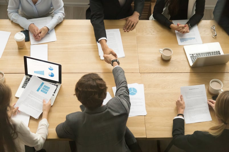 Legal team at boardroom table finalizes contract negotiations with a handshake.