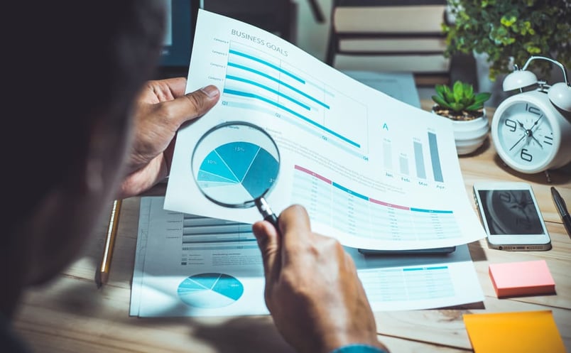 Businessman wondering what is contract analytics aiming magnifying glass at data sheet.